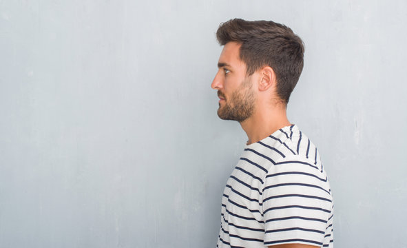Handsome young man over grey grunge wall wearing navy t-shirt looking to side, relax profile pose with natural face with confident smile.