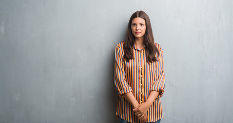 Young brunette woman over grunge grey wall with serious expression on face. Simple and natural looking at the camera.