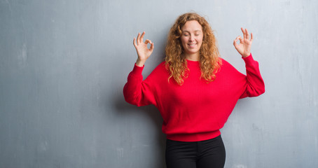 Young redhead woman over grey grunge wall wearing red sweater relax and smiling with eyes closed doing meditation gesture with fingers. Yoga concept.