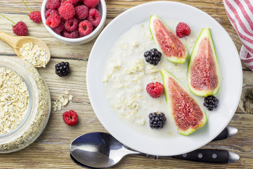 Bowl of oatmeal porridge with figs, raspberries and blackberries on teal rustic table