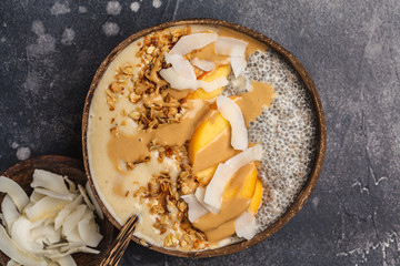 Smoothie bowl with chia pudding, peach, coconut and granola in a coconut bowl. Vegan healthy breakfast, clean eating concept.