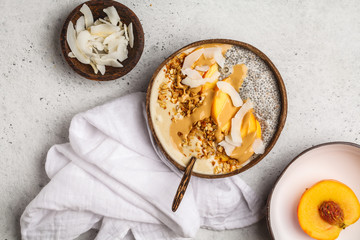 Smoothie bowl with chia pudding, peach, coconut and granola in a coconut bowl. Vegan healthy breakfast, clean eating concept.
