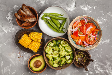 Clean eating concept. Cucumber salad, tomato salad, flax bread, avocado, corn. Top view, food background.