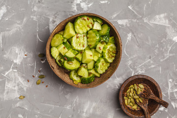 Simple cucumber salad in coconut bowl. Healthy vegetarian food. Top view, gray background.