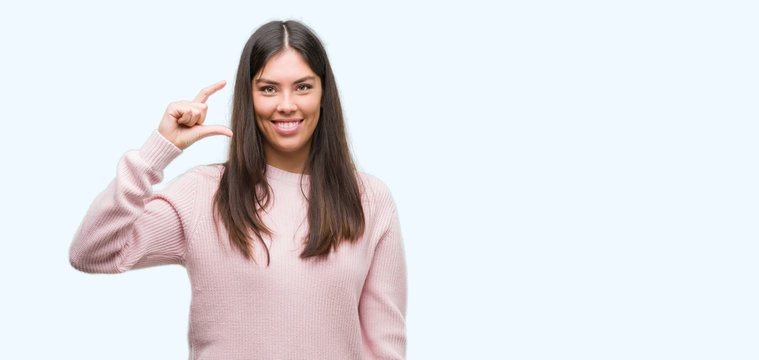 Young beautiful hispanic woman wearing a sweater smiling and confident gesturing with hand doing size sign with fingers while looking and the camera. Measure concept.
