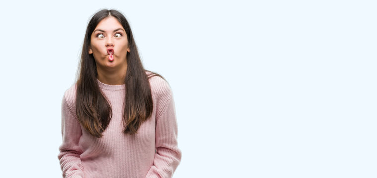 Young beautiful hispanic woman wearing a sweater making fish face with lips, crazy and comical gesture. Funny expression.