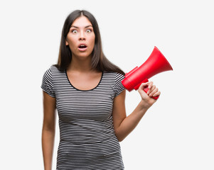 Young hispanic woman holding megaphone scared in shock with a surprise face, afraid and excited with fear expression