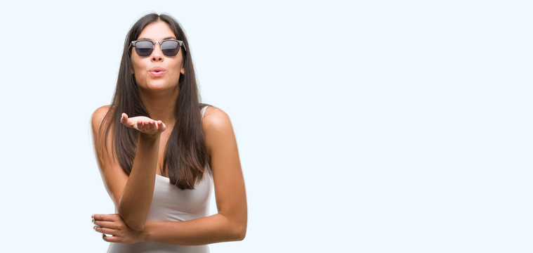 Young beautiful hispanic wearing sunglasses looking at the camera blowing a kiss with hand on air being lovely and sexy. Love expression.