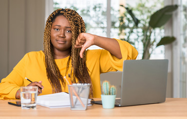 Fototapeta na wymiar African american woman studying with laptop with angry face, negative sign showing dislike with thumbs down, rejection concept
