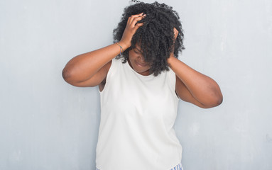 Young african american woman over grey grunge wall suffering from headache desperate and stressed because pain and migraine. Hands on head.