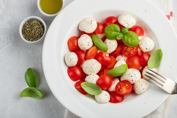 White plate of classic delicious caprese salad with ripe tomatoes, mozzarella and fresh basil leaves on gray concrete background. Italian food. The concept of a healthy vegetarian diet. Top view