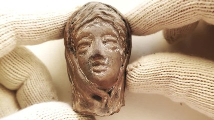 Archeologist inspects tiny ancient authentic clay head - Powered by Adobe