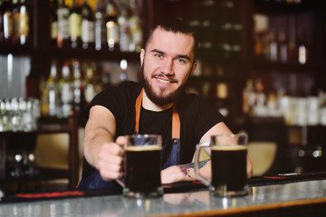 young cute barman with a mug of beer smiling at the bar background. Oktoberfest