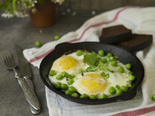 Delicious breakfast - fried eggs with green peas. On a dark background. Close up, copy space