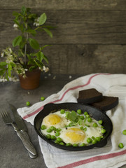 Delicious breakfast - fried eggs with green peas. On a dark background. Close up, copy space