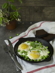 Delicious breakfast - fried eggs with green peas. On a dark background. Close up, copy space