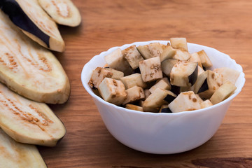 Eggplant, finely chopped for further preparation in a white plate on a wooden background, a number of slices of chopped fruit.