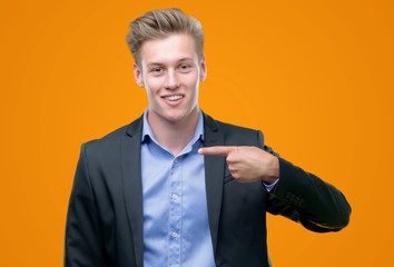 Young handsome blond business man with surprise face pointing finger to himself