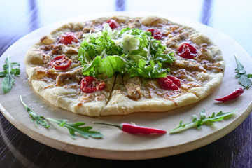 Pizza on a round wooden platter. Decorated with herbs and chili.