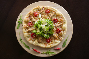 Pizza on a round wooden platter. Decorated with herbs and chili. Shooting vertically from above.