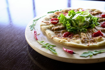 Pizza on a round wooden platter. Decorated with herbs and chili.