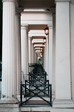 Diminishing perspective view of tall white columns, black iron cast fences, and antique lanterns of Victorian townhouses in London.