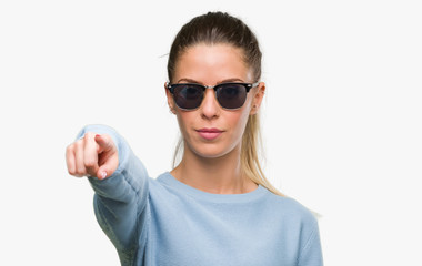 Beautiful young woman wearing sunglasses and ponytail pointing with finger to the camera and to you, hand sign, positive and confident gesture from the front