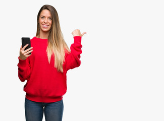 Naklejka premium Beautiful young woman using smartphone pointing with hand and finger up with happy face smiling