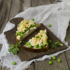 Bruschetta with green peas, cheese and egg on a wooden board. Close up, copy space