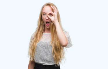 Fototapeta premium Blonde teenager woman wearing moles shirt doing ok gesture shocked with surprised face, eye looking through fingers. Unbelieving expression.