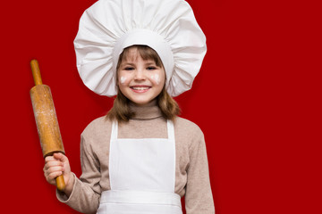 Happy little girl in chef uniform holds rolling pin isolated on light background. Kid chef. Cooking Process Concept 