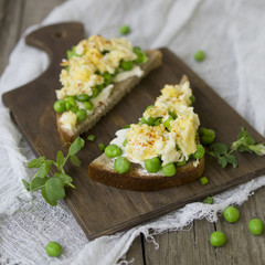 Bruschetta with green peas, cheese and egg on a wooden board. Close up, copy space
