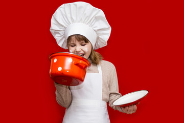 Happy little girl in chef uniform holds saucepan isolated on red. Kid chef. Cooking Process Concept