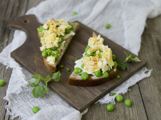 Bruschetta with green peas, cheese and egg on a wooden board. Close up, copy space