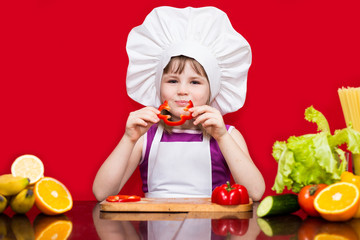 Happy little girl in chef uniform cuts vegetables in kitchen. Kid chef. Vegetarian. Cooking Process Concept