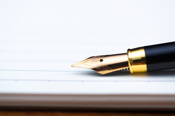 Close up of fountain pen or ink pen with notebook paper on wooden working table with copy space, office desk concept. shallow focus.