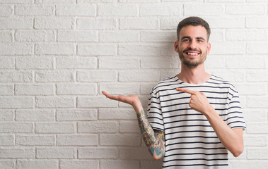 Young adult man standing over white brick wall very happy pointing with hand and finger