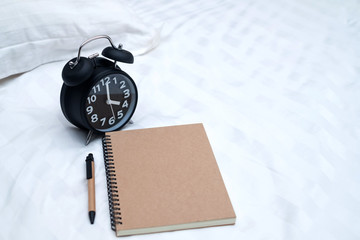 Diary or notebook and vintage alarm clock on bed in bedroom at home or hotel..
