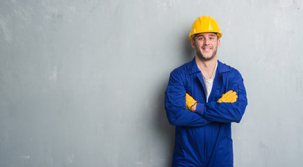 Young caucasian man over grey grunge wall wearing contractor uniform and safety helmet with a happy...