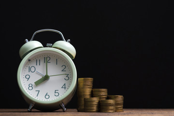 Alarm clock and coins stacks on working table in dark room, time for savings money concept, banking and business concept.