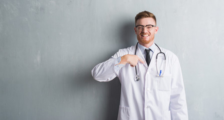Young redhead doctor man over grey grunge wall with surprise face pointing finger to himself