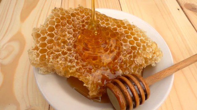 Honey dripping from honey dipper on honeycomb, over yellow background. slow motion