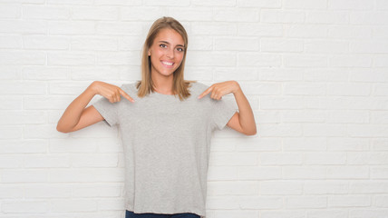 Beautiful young woman over white brick wall looking confident with smile on face, pointing oneself with fingers proud and happy.