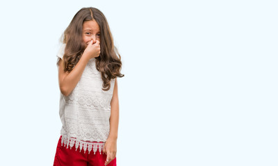 Brunette hispanic girl smelling something stinky and disgusting, intolerable smell, holding breath with fingers on nose. Bad smells concept.