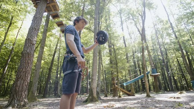 Professional climber in adventure park like a boss portrait shot 4K. Low angle wide view slow motion of young guy in focus wearing climbing equipment put down helmet and look over the right shoulder