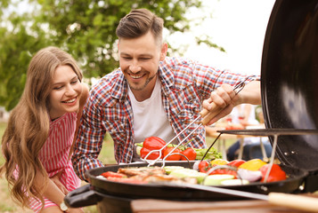 Young couple having barbecue with modern grill outdoors