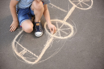 Little child drawing car with chalk on asphalt