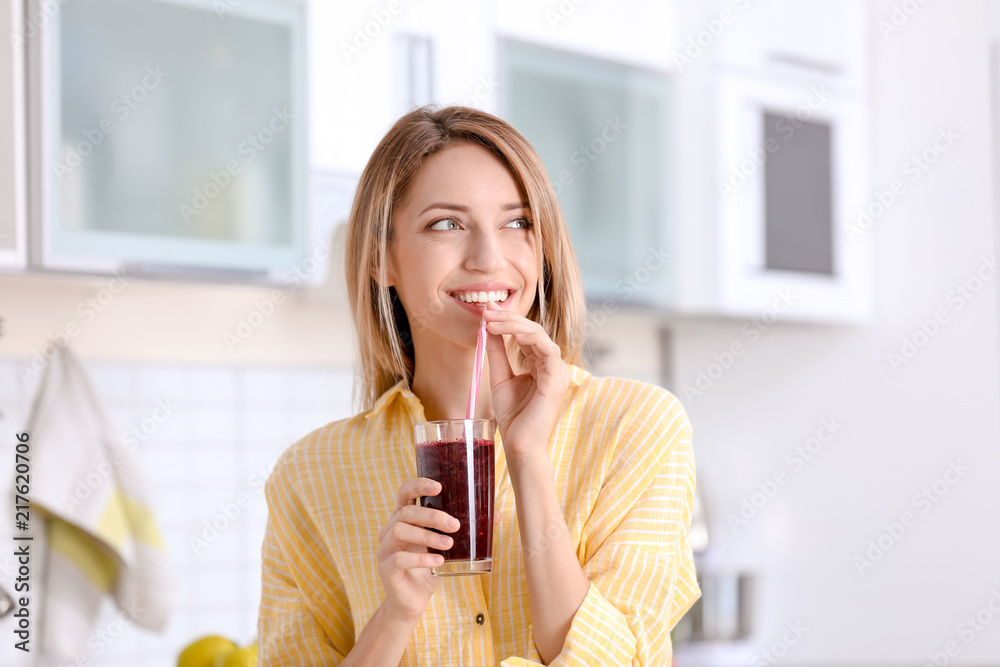 Wall mural young woman with glass of tasty healthy smoothie in kitchen