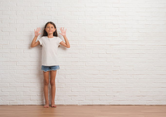 Young hispanic kid stading over white brick wall showing and pointing up with fingers number ten while smiling confident and happy.