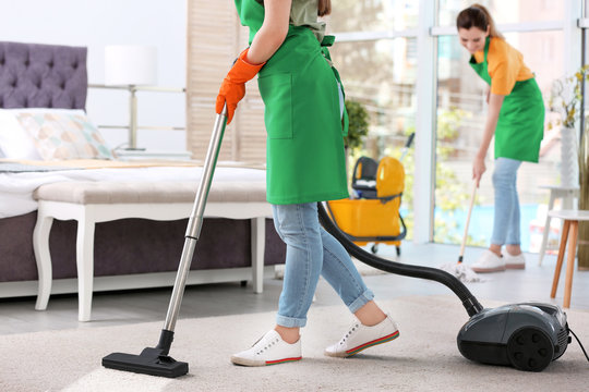 Woman removing dirt from carpet with vacuum cleaner in bedroom